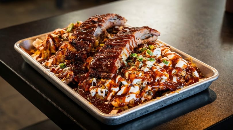 BBQ ribs and loaded fries with sauce, sour cream, and green onions on a metal tray.