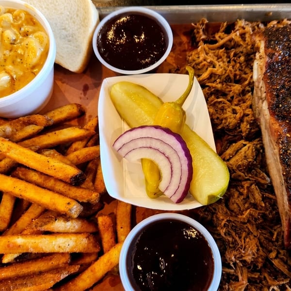 Barbecue platter with pulled pork, ribs, fries, mac and cheese, pickles, onions, and BBQ sauce.